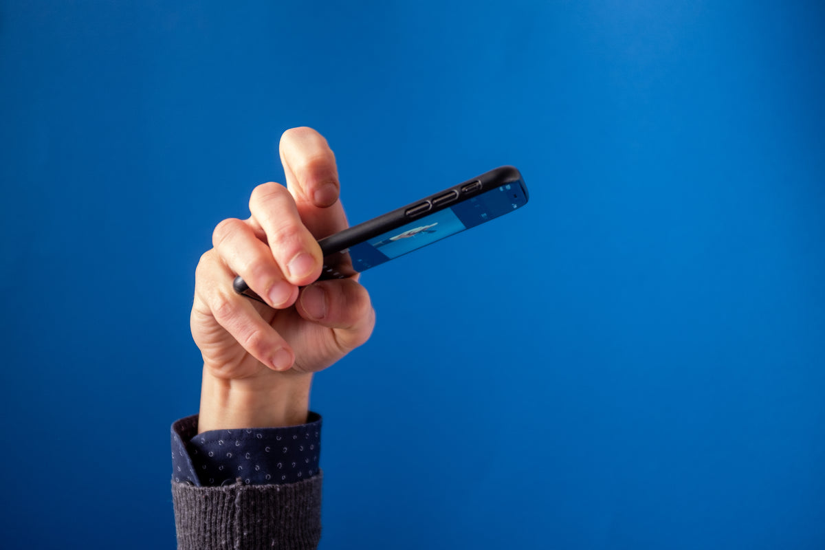 A hand holds a smartphone displaying a gallery of photographs against a blue background.
