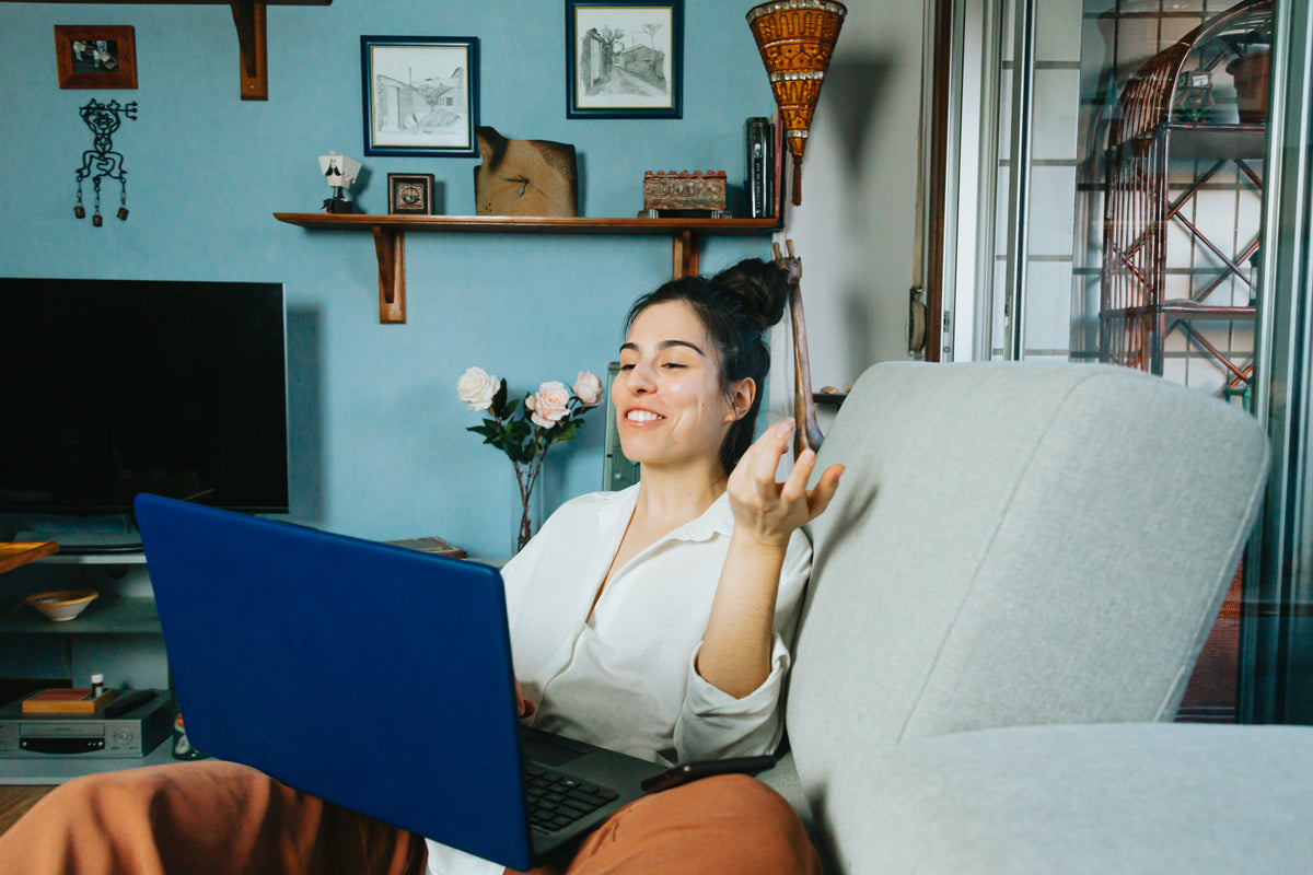 A person wearing earbuds gestures toward an open laptop while seated at home.