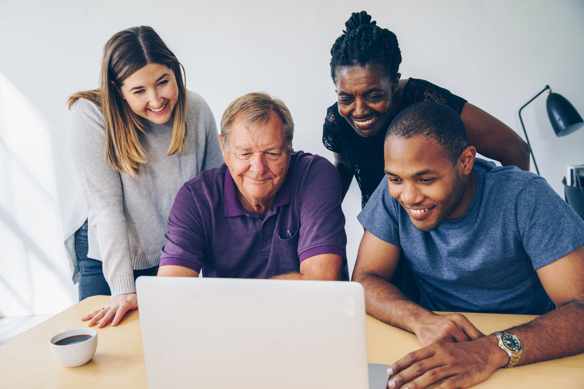 Four people gather around a laptop at a table.