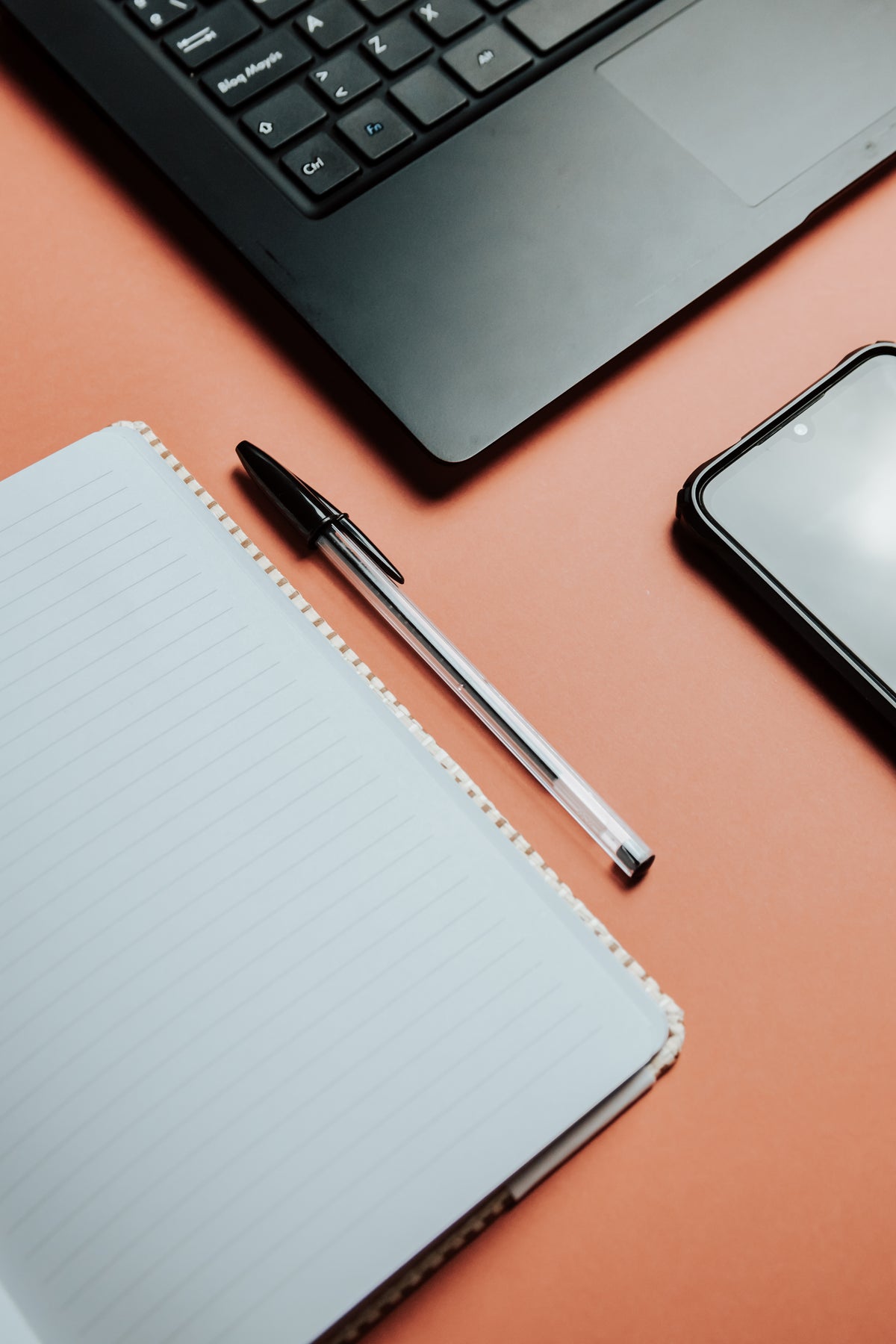 A lined notebook and pen sit beside a laptop and phone.