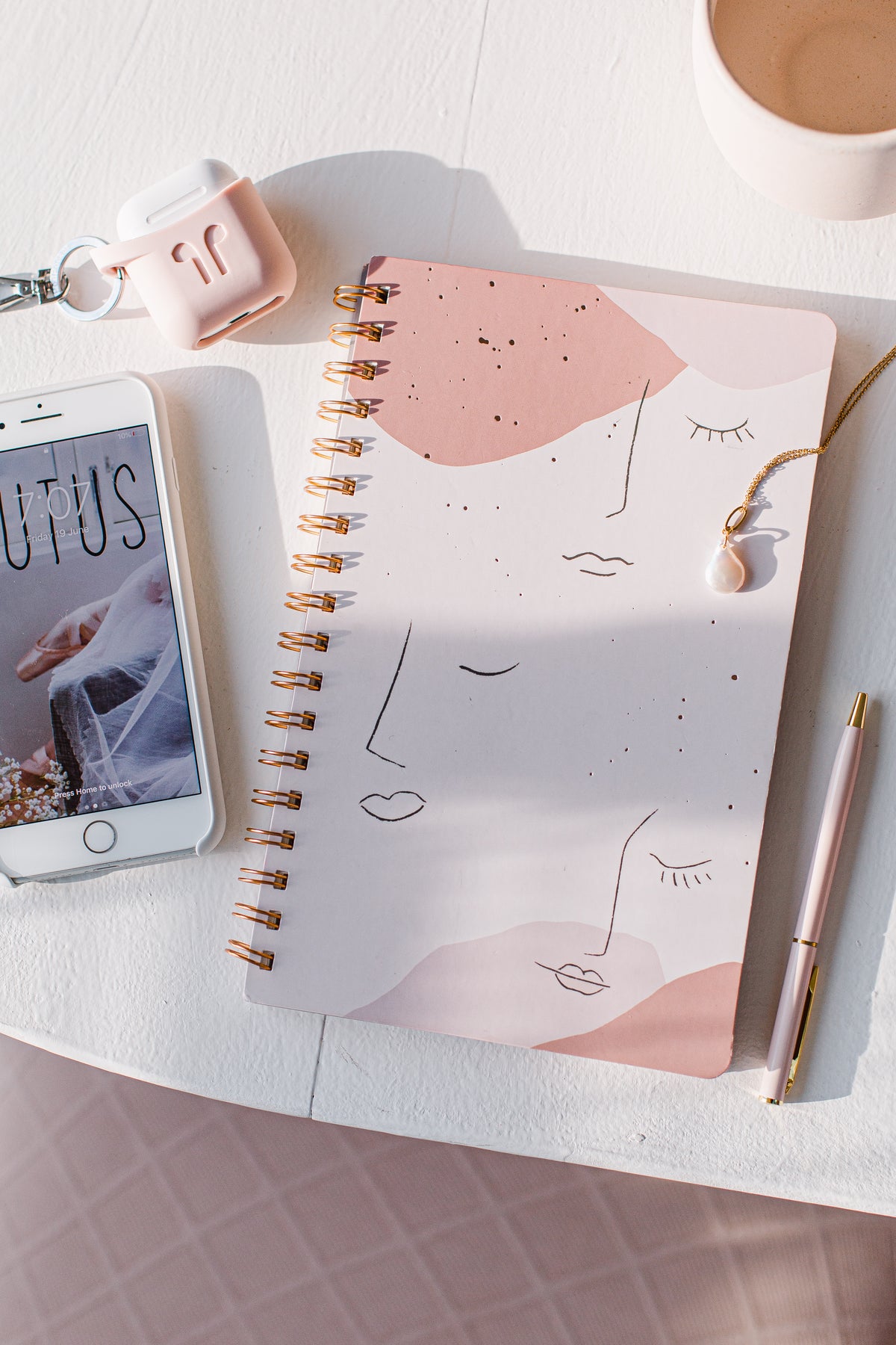 A phone, spiral notebook, and pen arranged on a light desk.