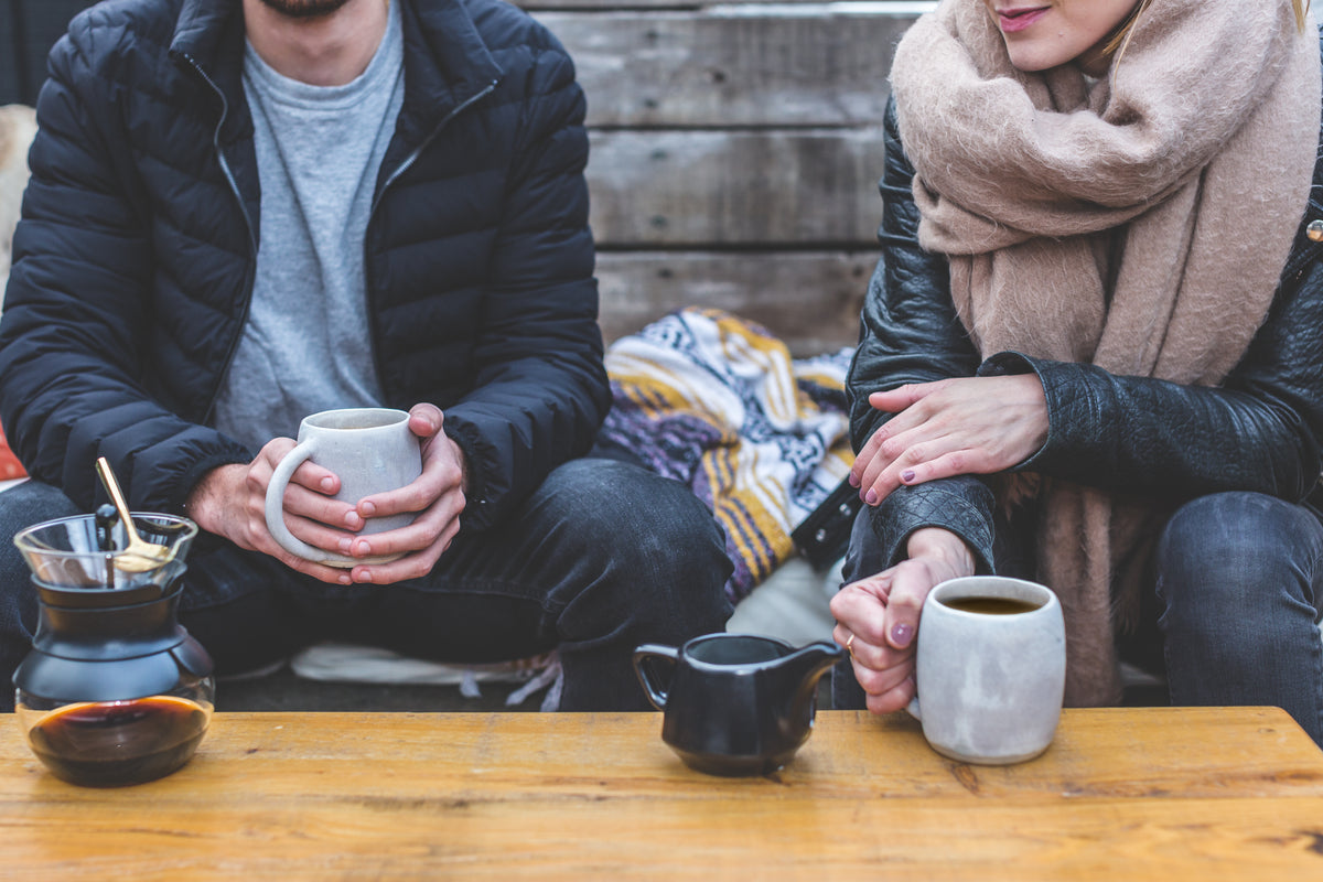 Two people sit together with coffee mugs at a wooden table.