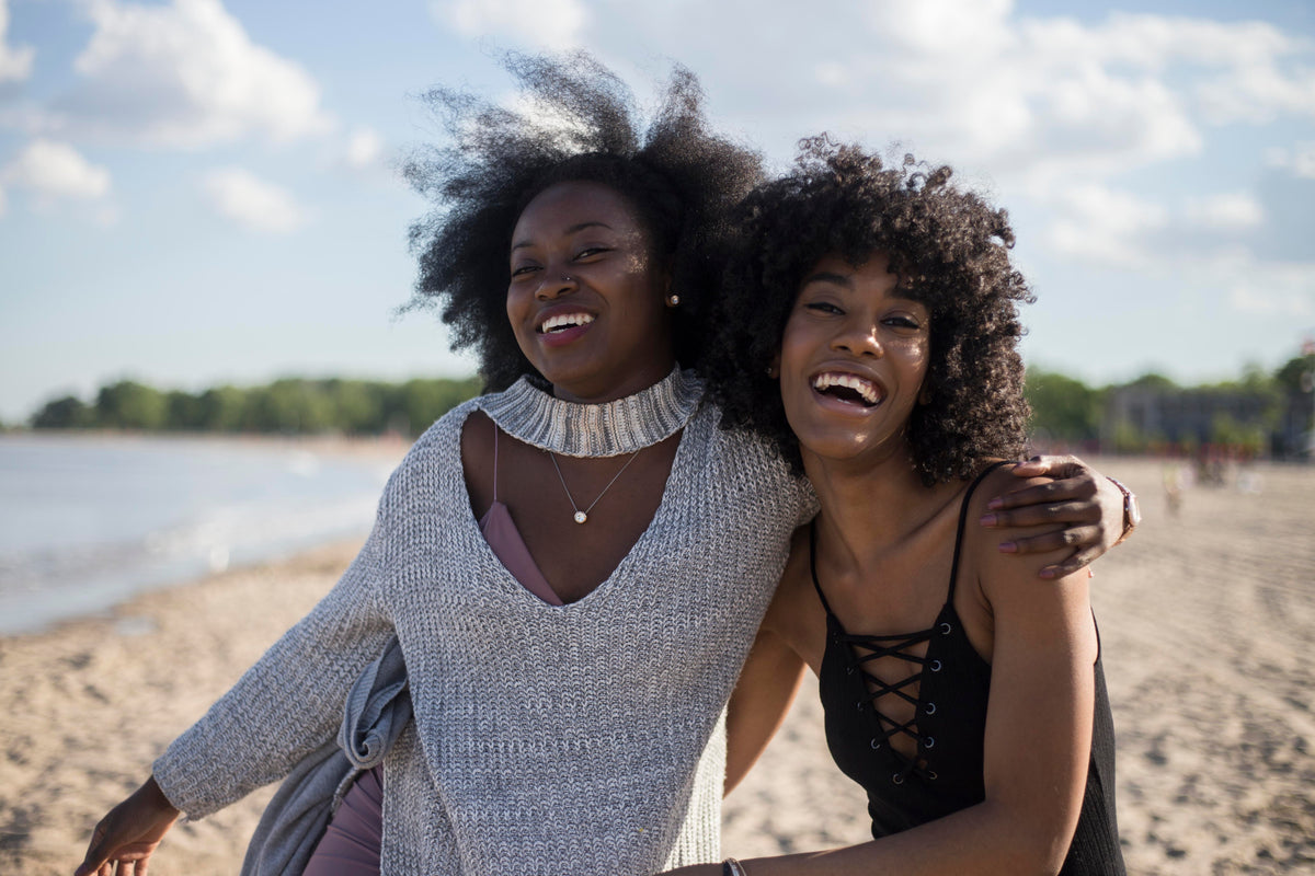 Two friends smile together at a beach.