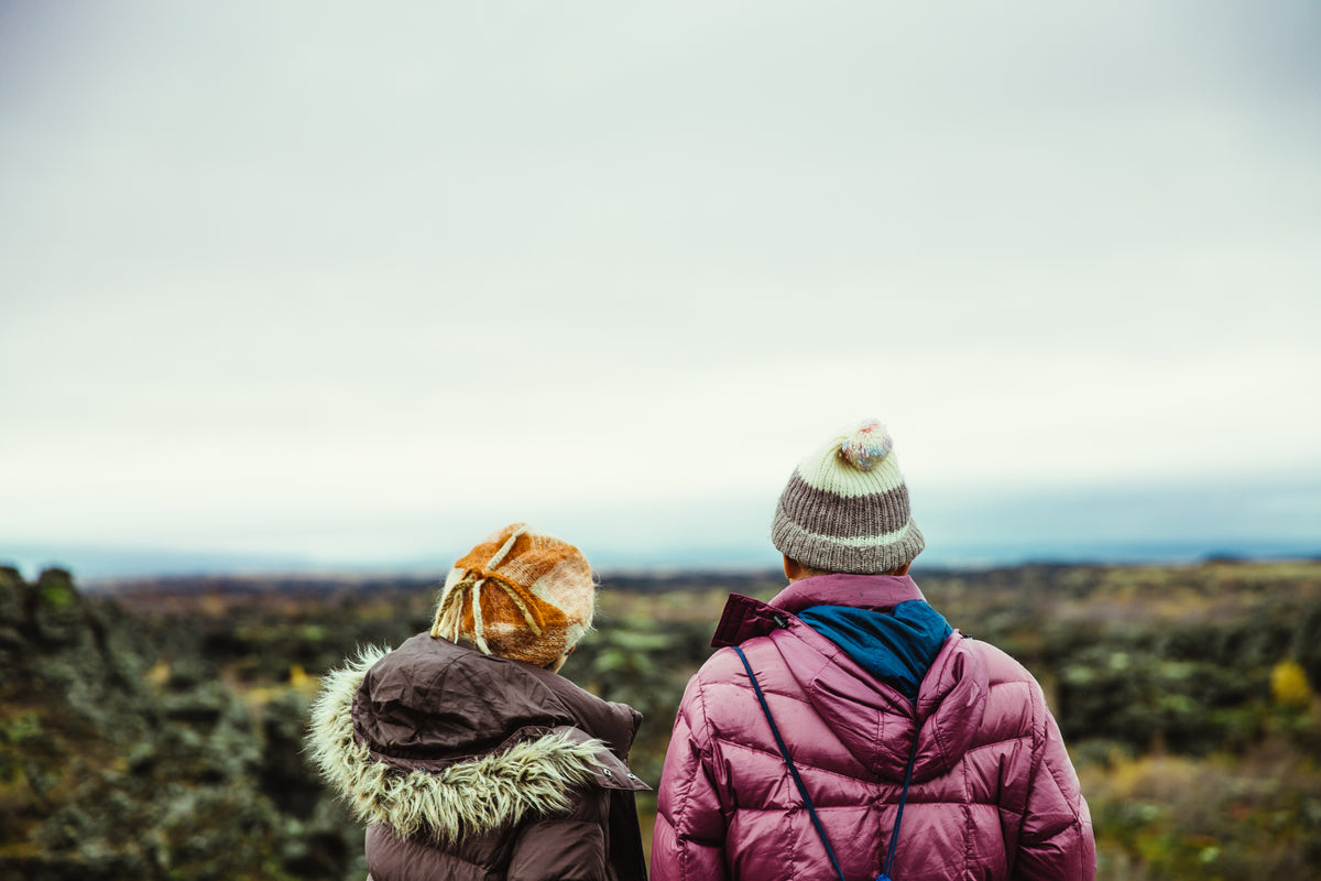 Two people in winter clothing look across an outdoor landscape.