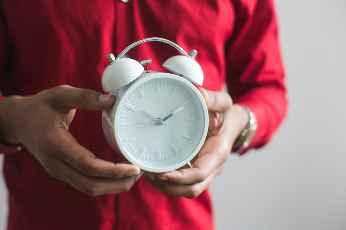 Hands holding a white alarm clock in front of a red shirt
