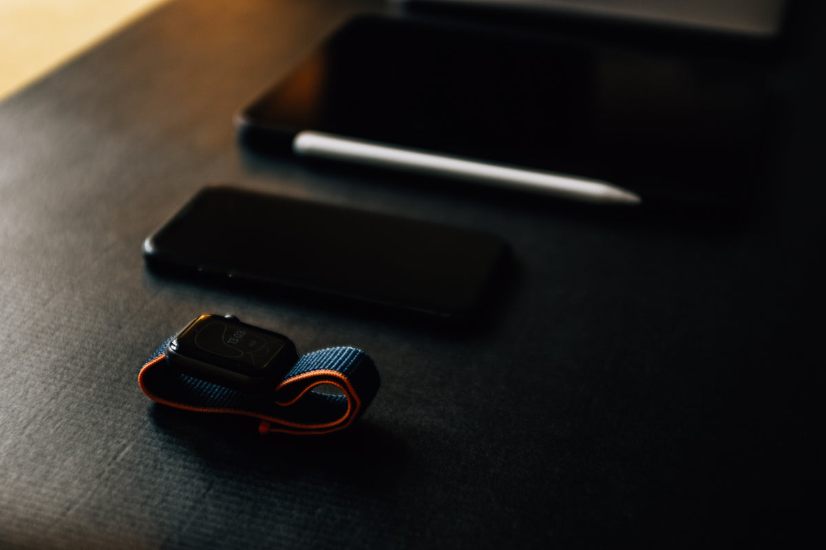 A smartwatch, smartphone, and tablet rest on a black table.