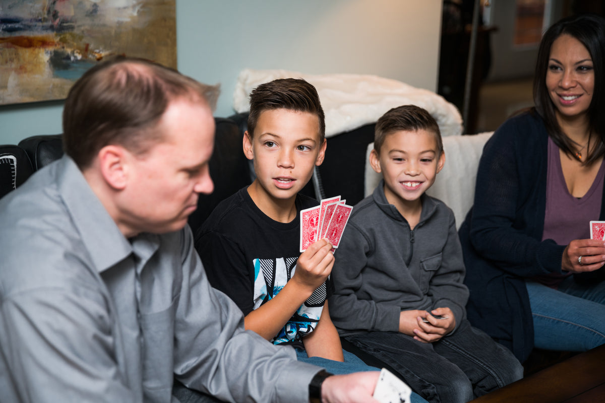 A family sits together on a couch playing a card game.