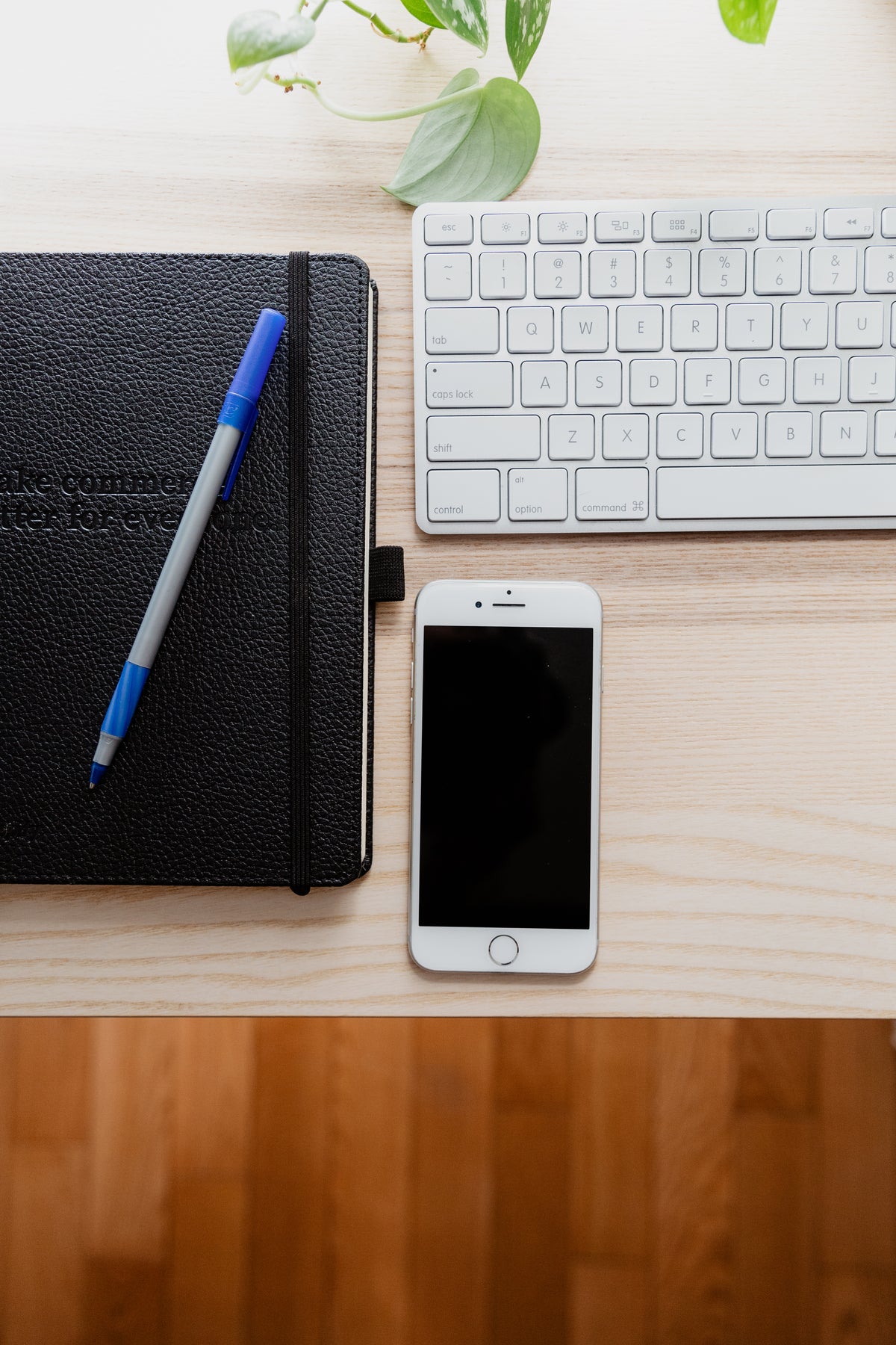 A white smartphone and black leather notebook rest together on a desk.