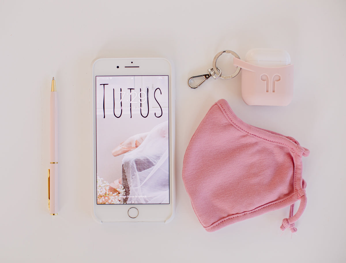 A smartphone, headphones, and travel items arranged on a pink surface.