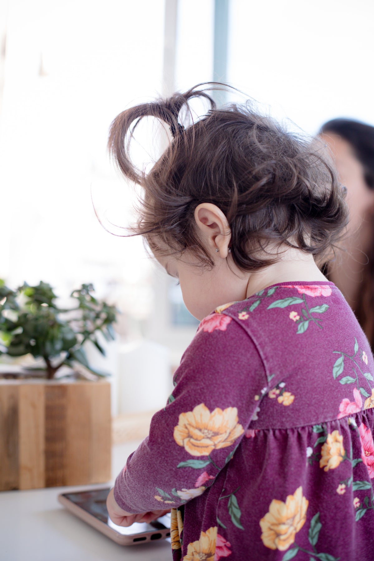 A child sits at a white table and looks toward a smartphone.
