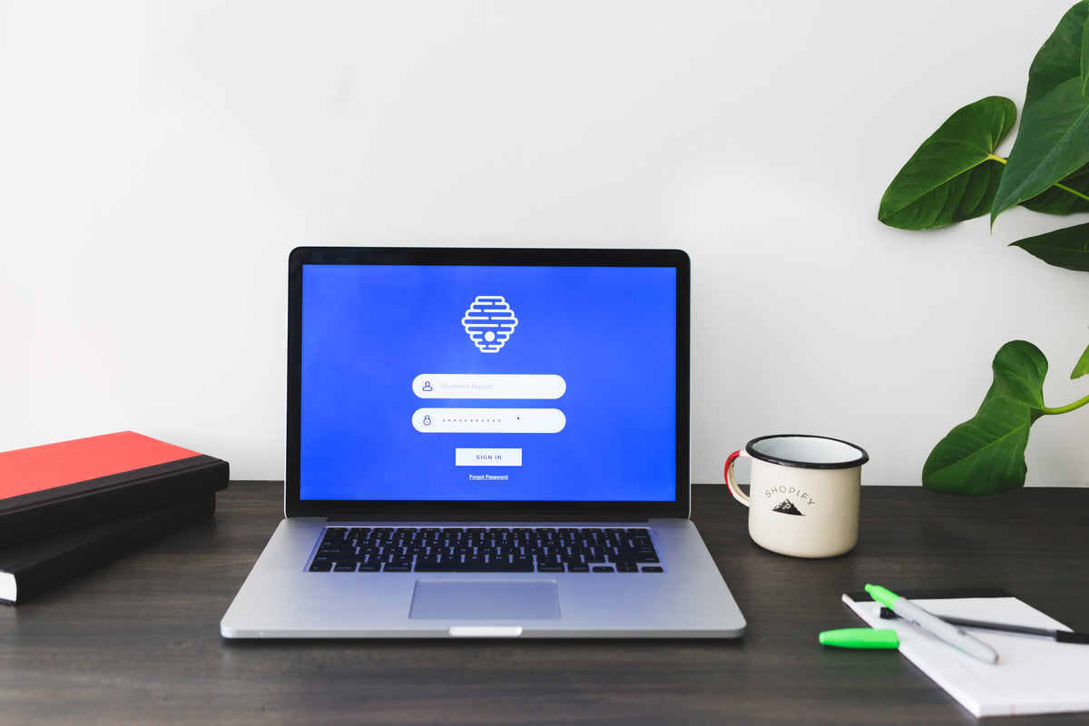 A laptop displays a login screen on a desk beside a mug.