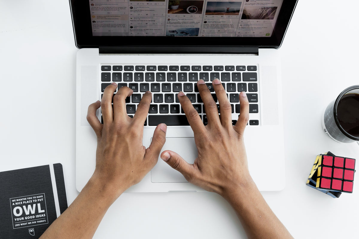 Overhead view of hands typing on a laptop on a white desk.