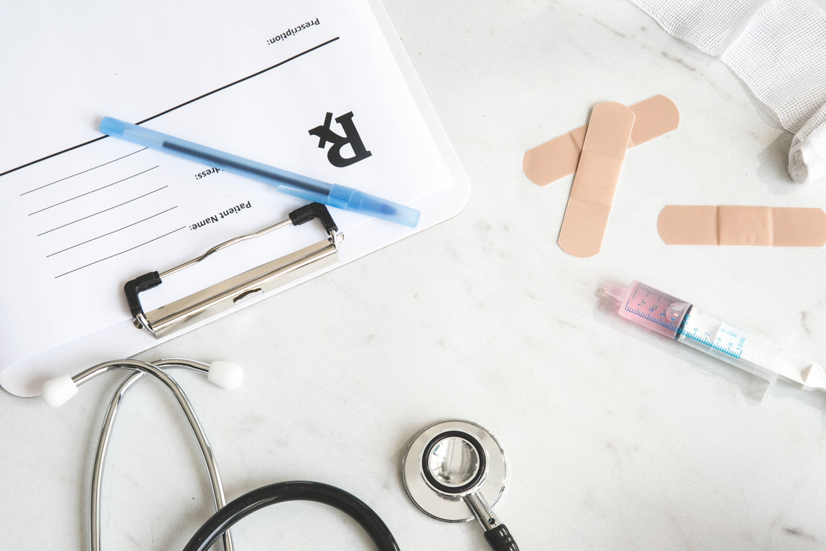 A clipboard, stethoscope, pencil, and medical supplies arranged on a white surface.
