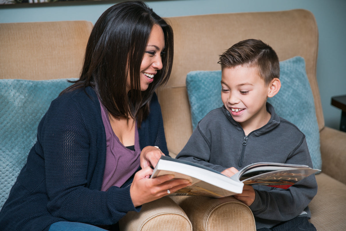 An adult and a child read a book together on a sofa.