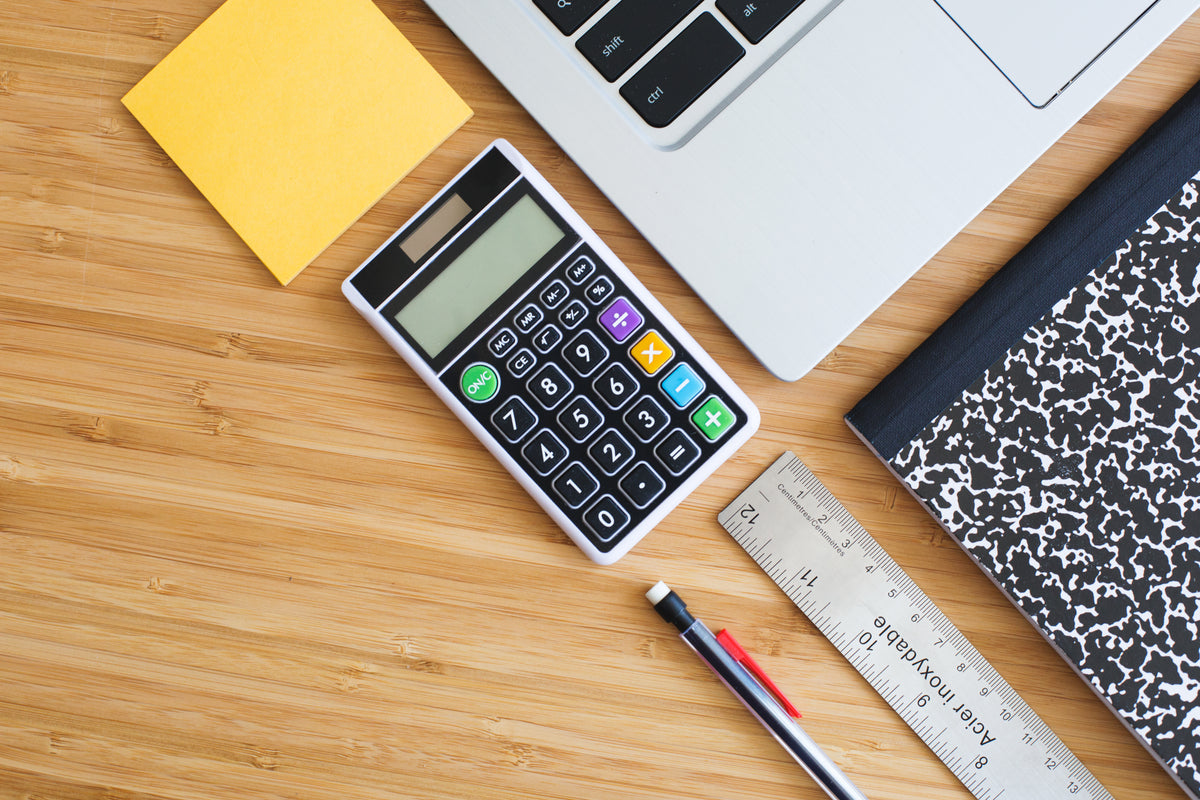 Study supplies including a calculator, notebook, ruler, and laptop on a desk.