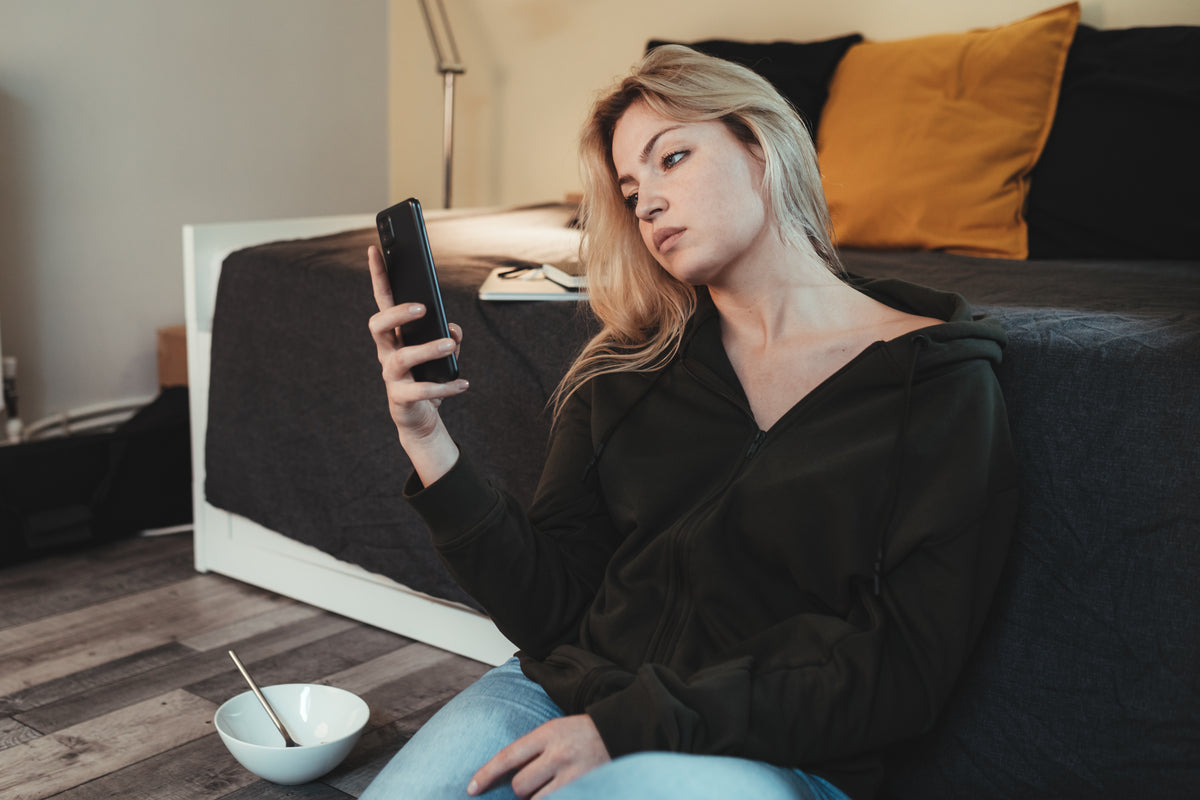 A woman seated beside a sofa looks at her phone.