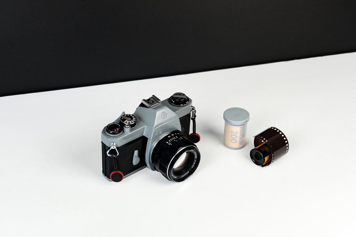 A film camera and film canisters rest on a light surface.