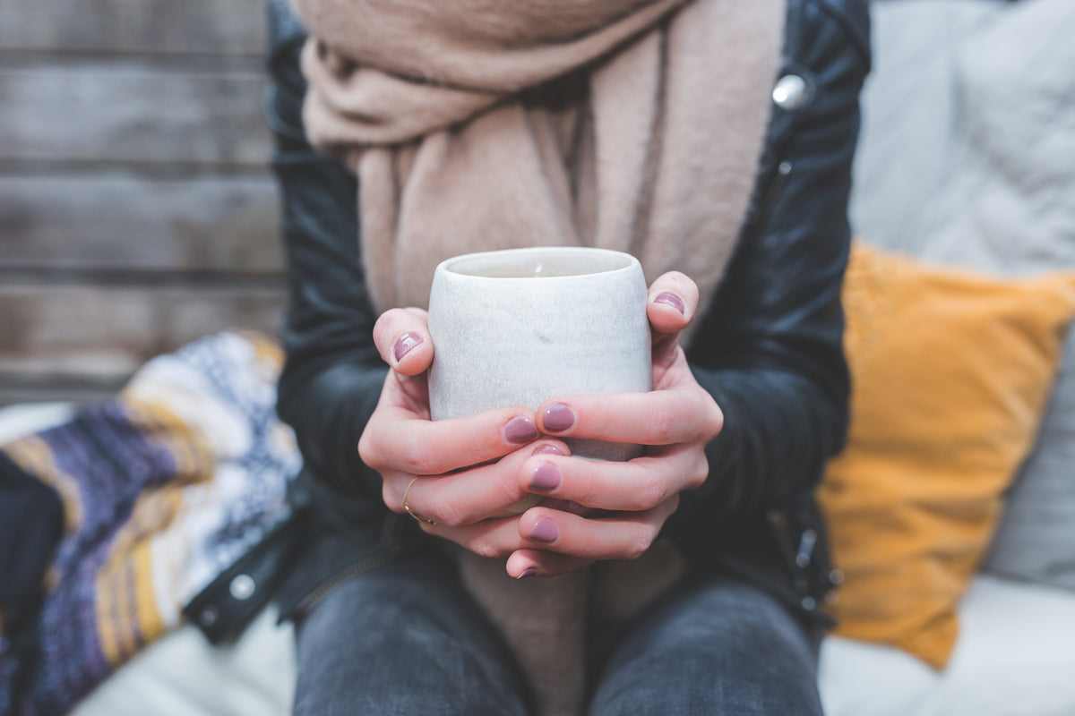 A person holds a white mug in both hands.