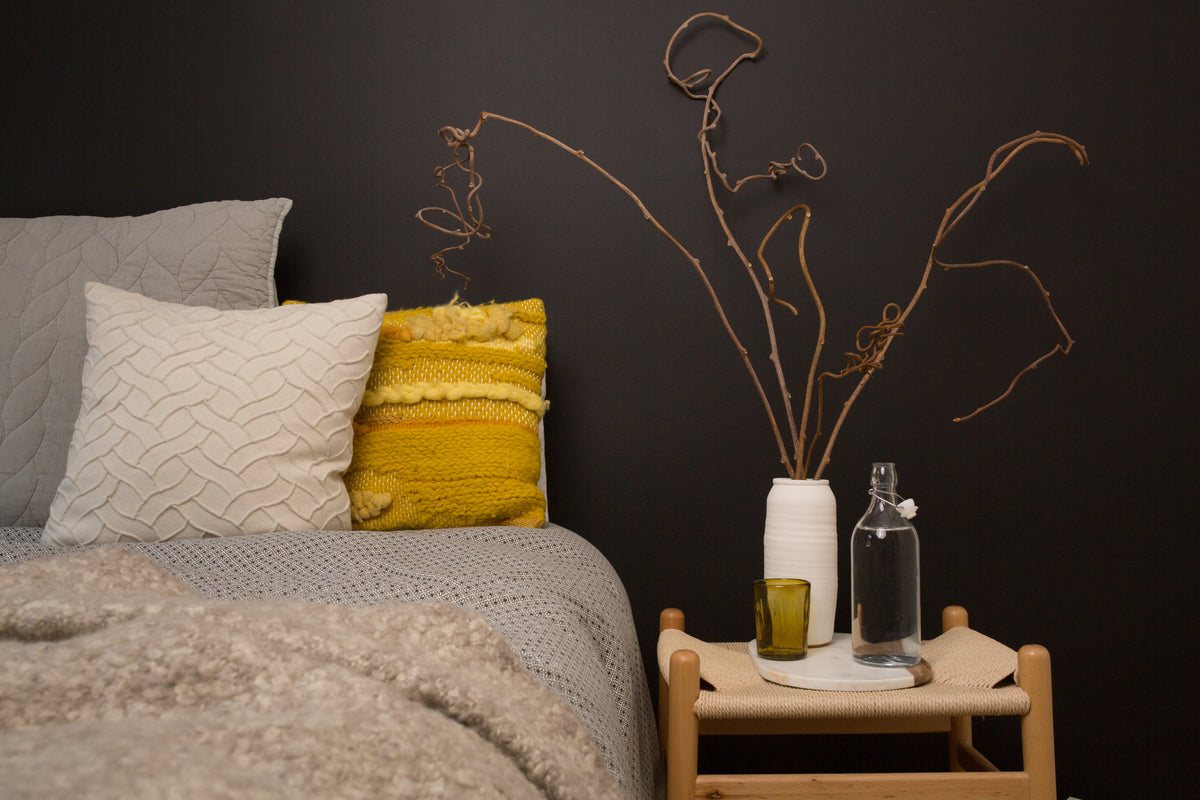 A bed with a yellow pillow beside a small bedside table.