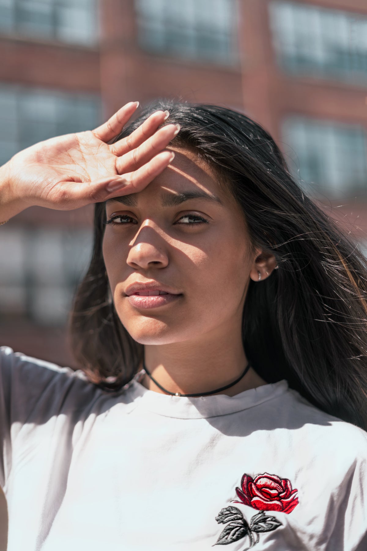 A woman outdoors raises one hand to shade her face from sunlight.